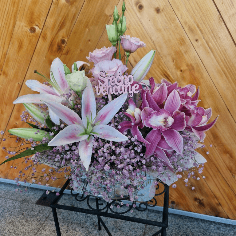 Cvetni aranzman u kombinaciji ružičastih ljiljana, orhideja, lisianthusa i roze gipsofile upotpunjena je elegantnim natpisom Srećno venčanje